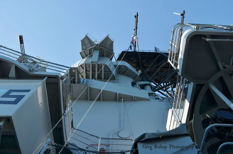 View looking up at the superstructure and radar equipment of a large naval ship under a clear blue sky, with metal railings and wires visible in the foreground—a striking scene you might experience at the Los Angeles museum dedicated to maritime history.