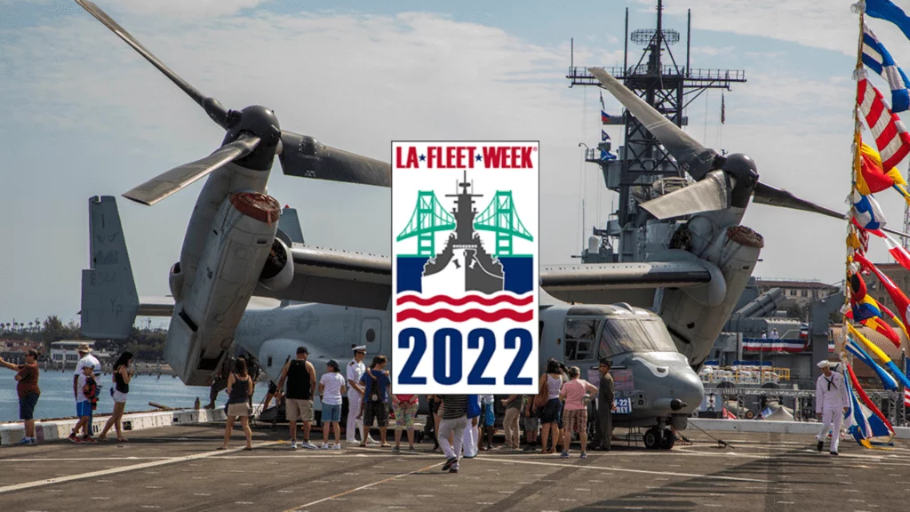 A crowd gathers near a military aircraft on a ship deck during LA Fleet Week 2022. The event logo with a ship and bridge is centered over the image. Colorful flags and another ship are visible in the background. A crowd gathers near a military aircraft on a ship deck during LA Fleet Week 2022. The event logo with a ship and bridge is centered over the image. Colorful flags and another ship are visible in the background.