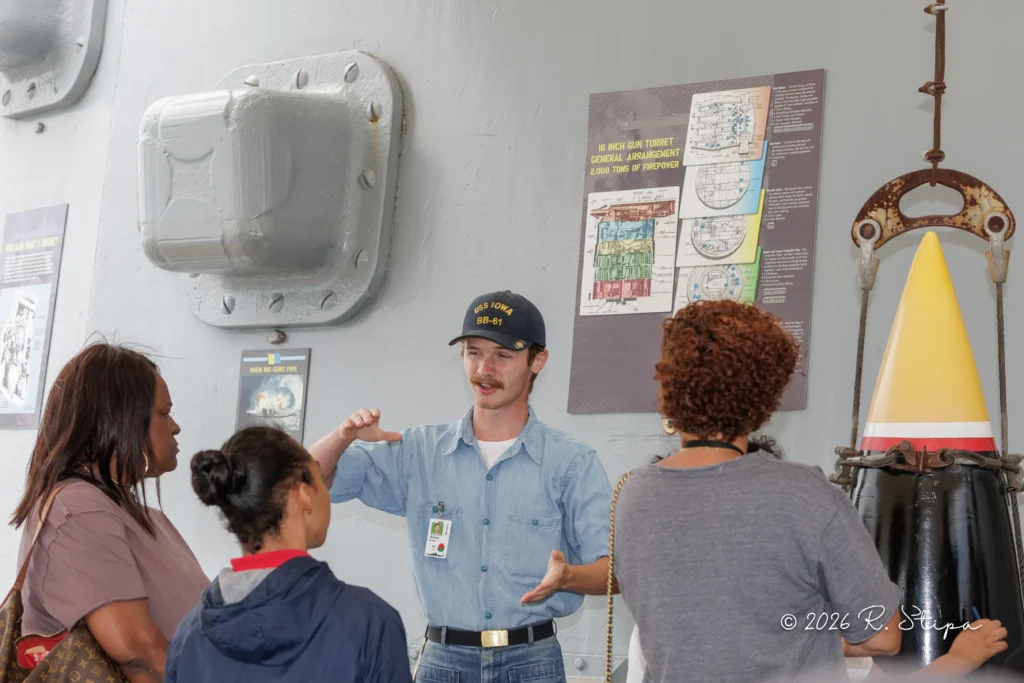 A museum guide offers an engaging overview to a small group near a large shell display and informational posters. One woman takes notes while others listen attentively, enhancing their experience of the exhibit.
