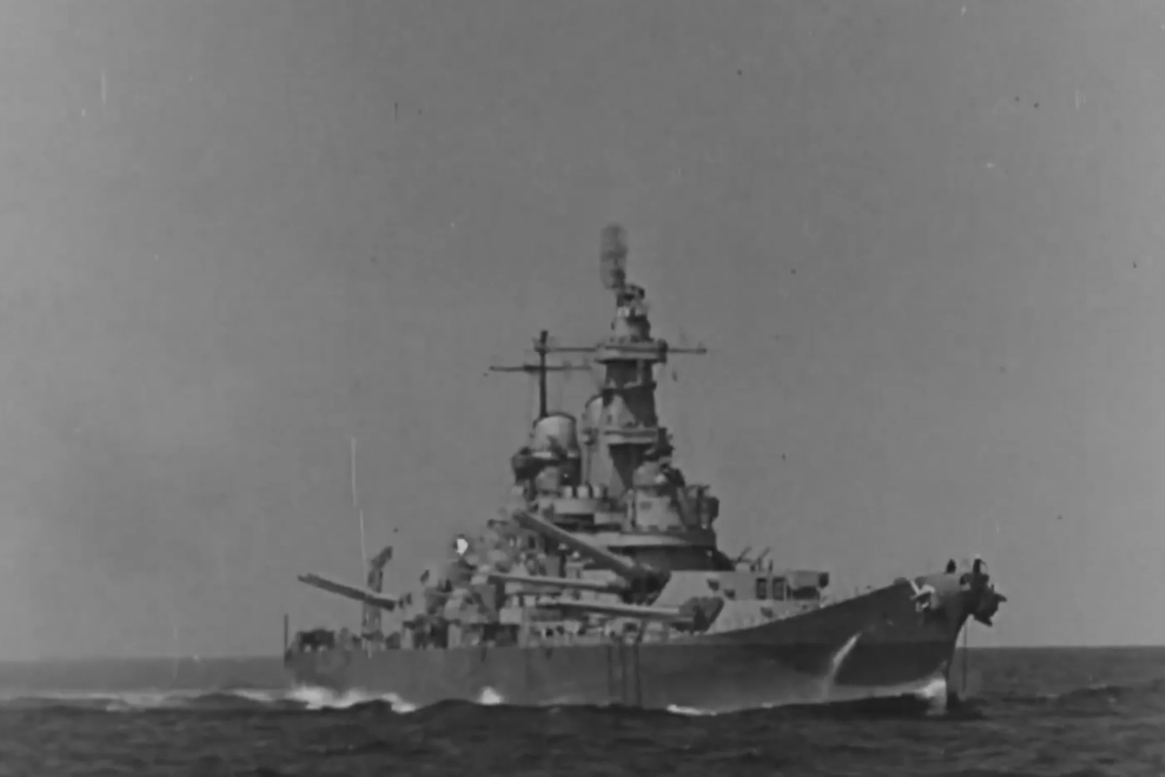 A large battleship sails on the open sea under a clear sky, proudly representing America 250. The ship features multiple gun turrets and various radar and communication equipment mounted on its superstructure. A large battleship sails on the open sea under a clear sky, proudly representing America 250. The ship features multiple gun turrets and various radar and communication equipment mounted on its superstructure.