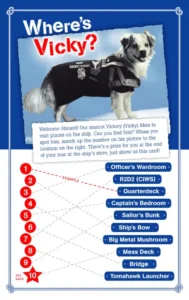 A dog wearing a black jacket sits on a ship-themed game board with numbered circles and a list of ship locations, titled Wheres Vicky? at the top.