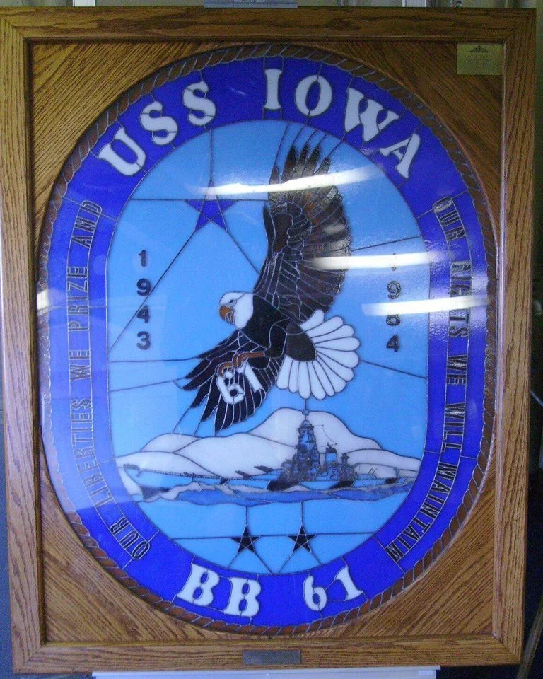 Stained glass plaque for USS Iowa BB 61 with a bald eagle, ship, and mountains. Includes years 1943 and 1984, and a border inscription honoring battles and crew—a striking centerpiece perfect for museum exhibits dedicated to the iconic battleship.